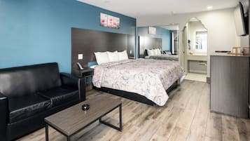 A modern hotel room with a bed, a black leather sofa, a wooden coffee table, and a desk with a mirror.