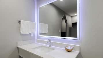Une salle de bain moderne avec un lavabo blanc, un miroir et deux serviettes blanches accrochées au mur.