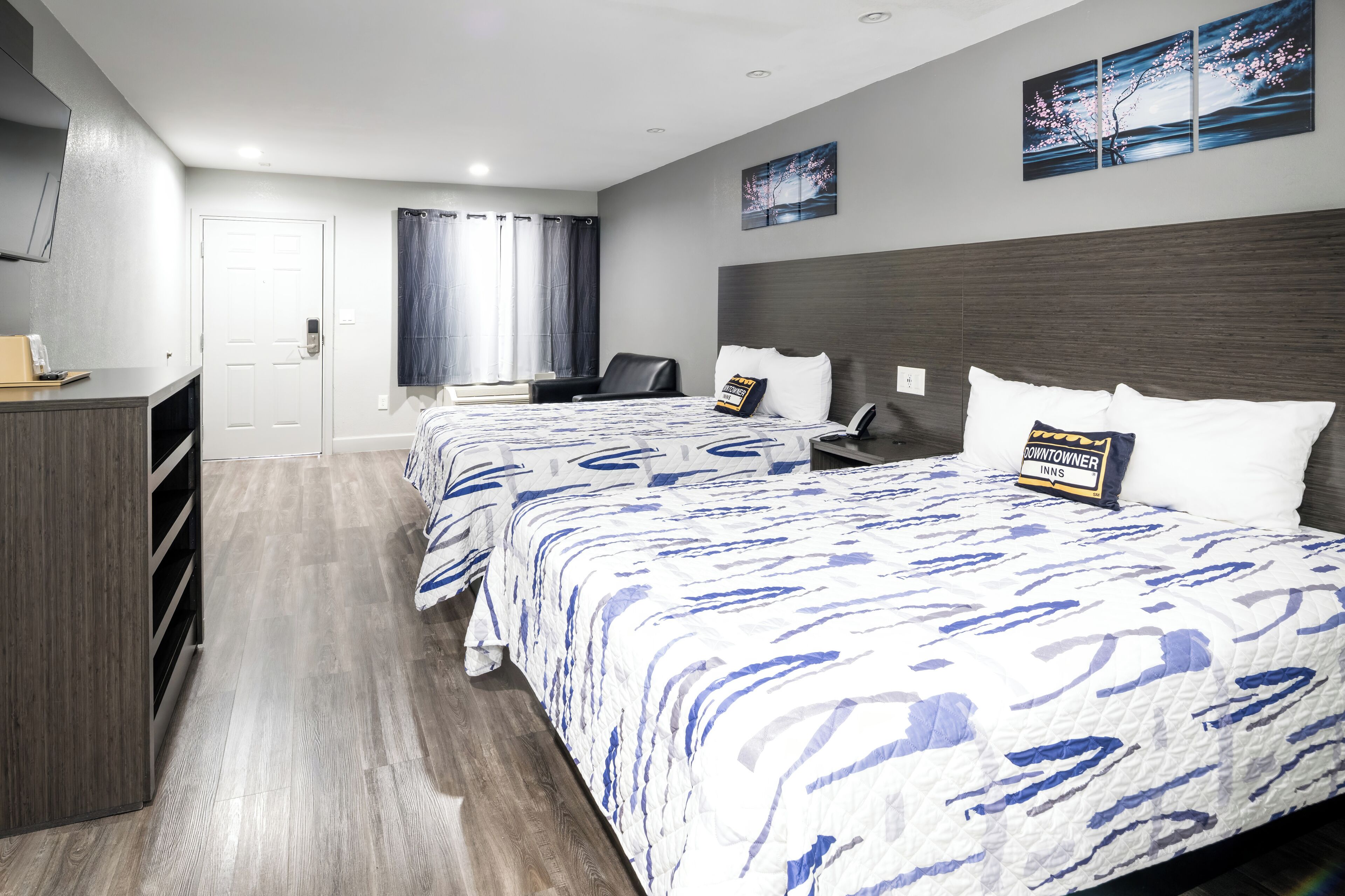 Ein Hotelzimmer mit zwei Betten, einem Schreibtisch, einem Sessel, einem Fernseher und Bildern an den Wänden.