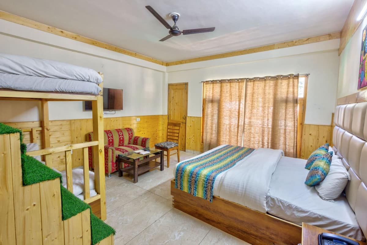 Una habitación con literas, un sofá, una silla, una mesita pequeña y una cama con una colcha a rayas.