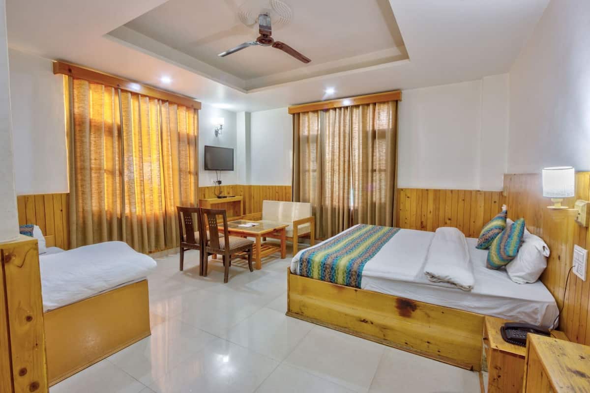 Una habitación de hotel con dos camas individuales, un escritorio de madera, una silla, un televisor y un ventilador de techo.