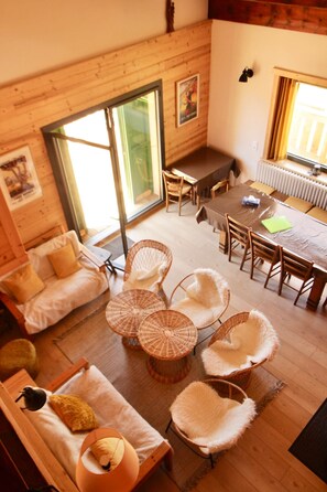 Una stanza accogliente con pavimento in legno, un divano, un tavolo da pranzo con sedie e un'ampia finestra.