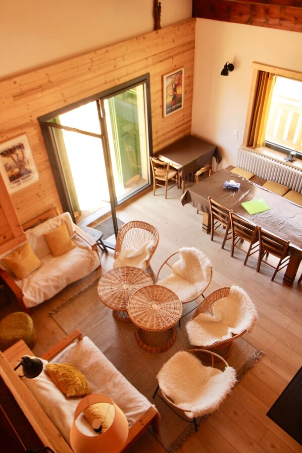 A cozy room with a wooden floor, a sofa, a dining table with chairs, and a large window.