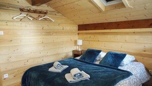 Un dormitorio de cabaña de madera con cama, dos almohadas, una colcha y una mesita de noche con lámpara.