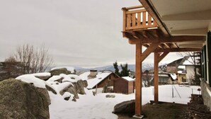 Una estructura de madera con un balcón que da a un paisaje nevado con casas y montañas al fondo.