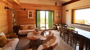 Un interior de madera con un sofá, sillas de mimbre, una mesa de comedor y una estantería.