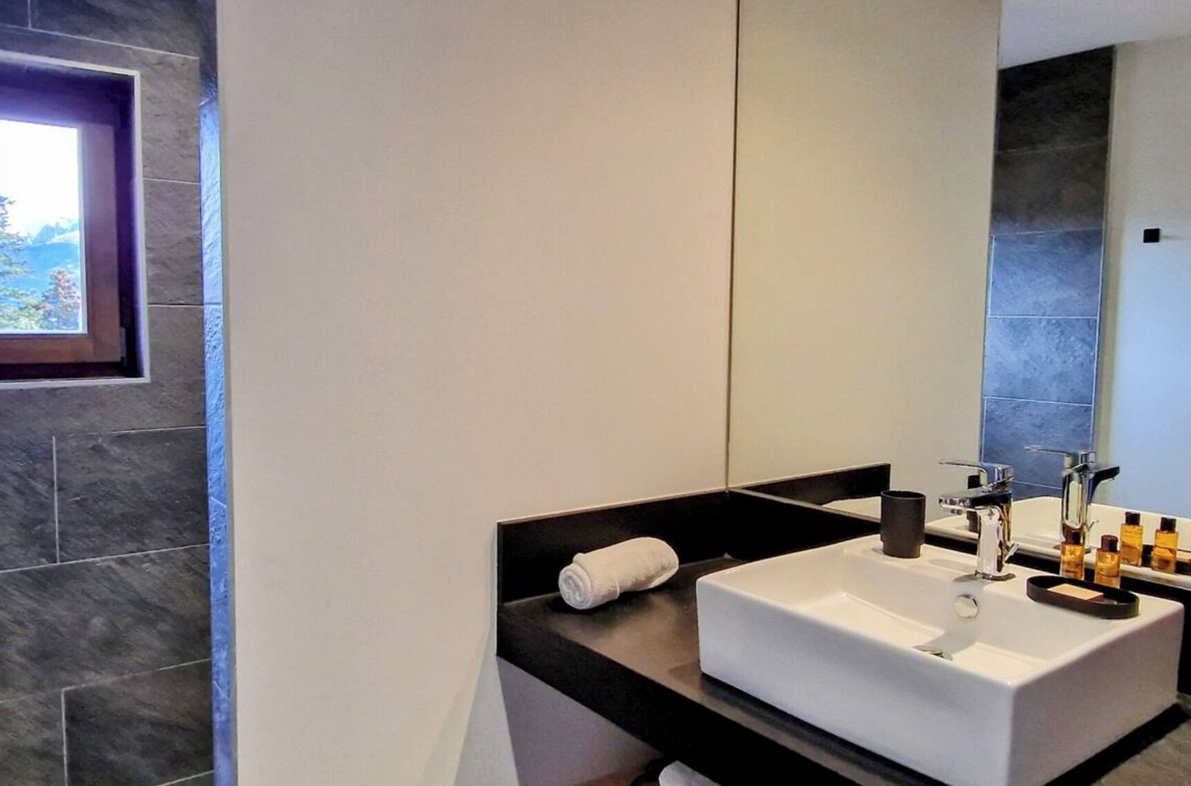 A modern bathroom with a large mirror, a white sink, and a black countertop.