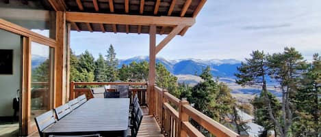 A wooden deck with a table and chairs, overlooking a mountainous landscape.
