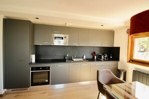 A modern kitchen with grey cabinets, a built-in oven, a microwave, and a glass dining table.