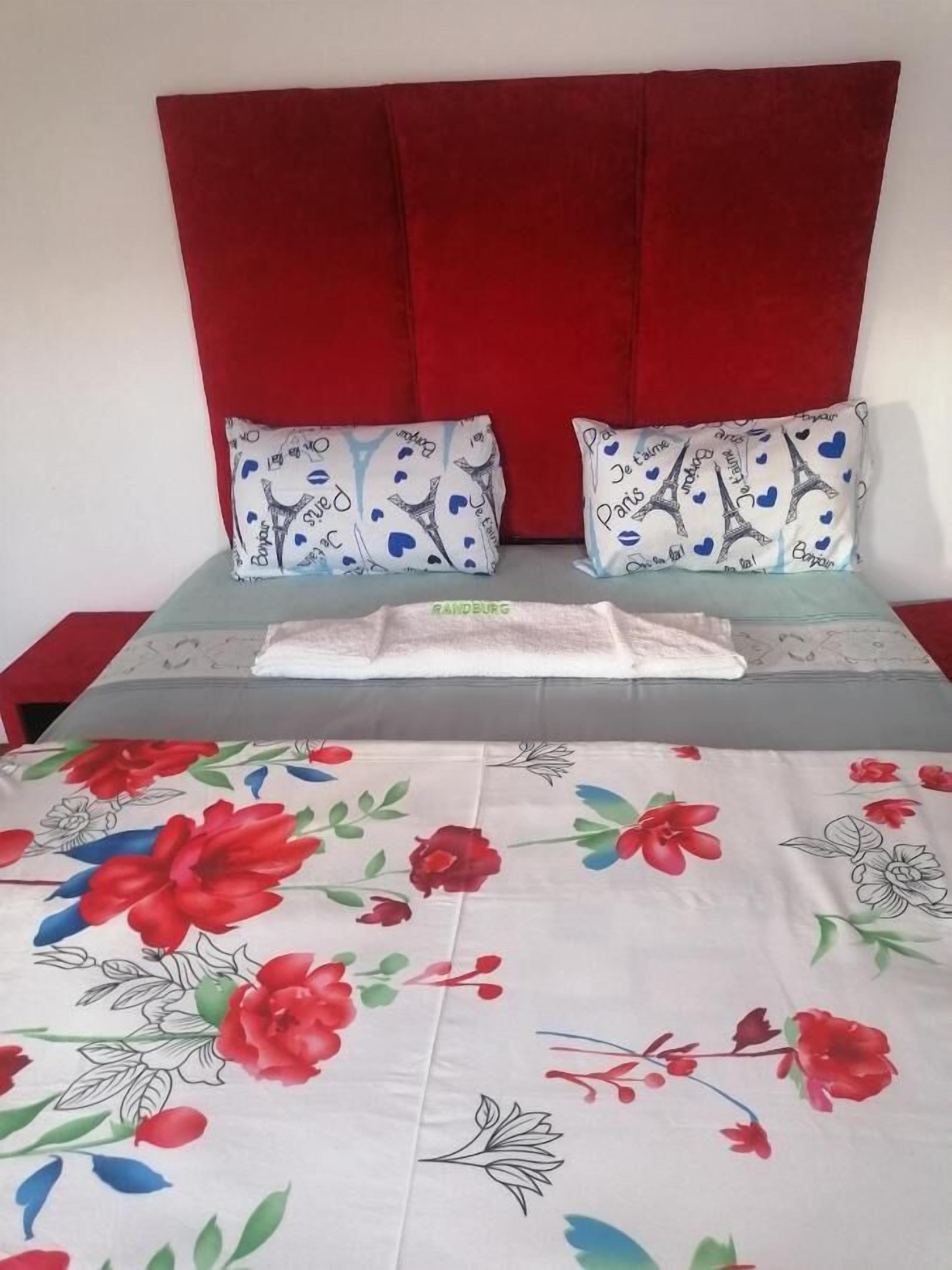 Una cama con cabecera roja, dos almohadas decorativas y una colcha estampada.