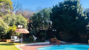 Un jardin avec une piscine, une terrasse en briques et une pelouse.