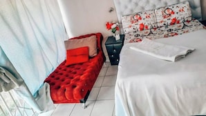 A bedroom with a large bed, a red tufted sofa, a nightstand, and a window with curtains.