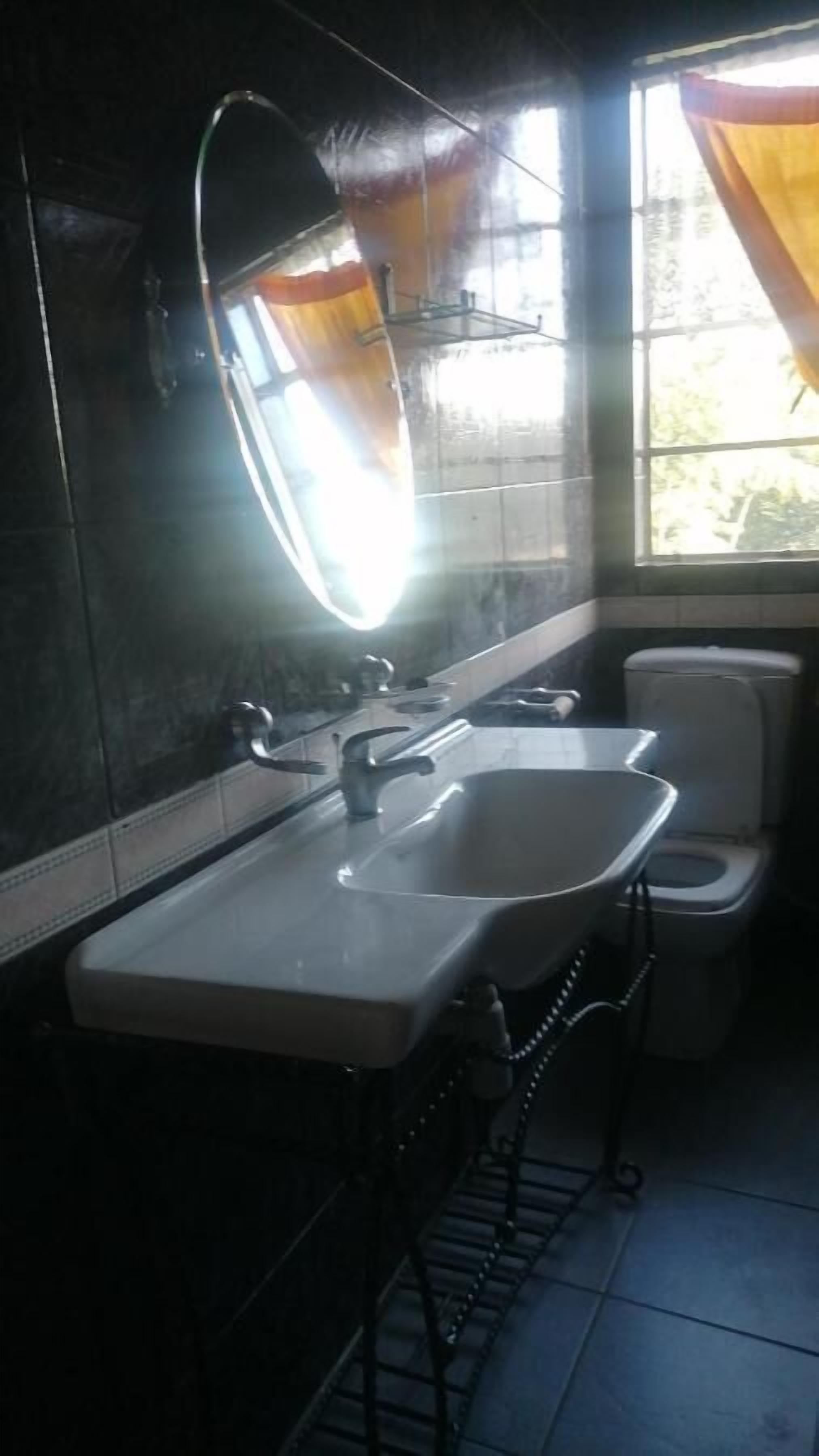 A bathroom with a large mirror, two sinks, a toilet, and a window with curtains.