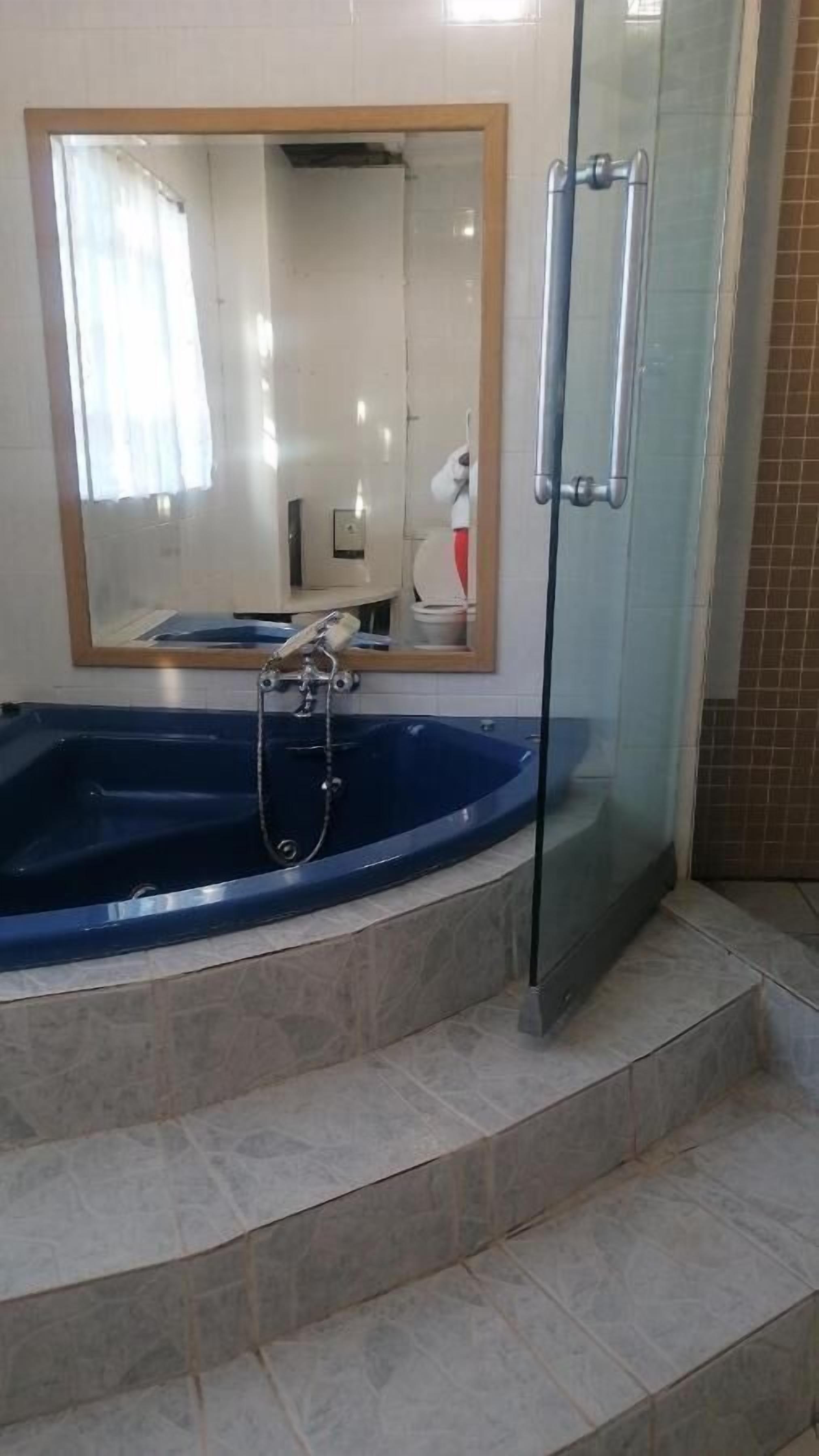 Un baño con una bañera azul grande, un box de ducha de cristal y un espejo sobre la bañera.