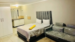 A bedroom with a bed, a sofa, a wardrobe, and a bathroom visible in the background.