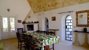Une salle à manger avec une table dressée pour six personnes, entourée de chaises, d’une cheminée et d’un grand miroir au mur.