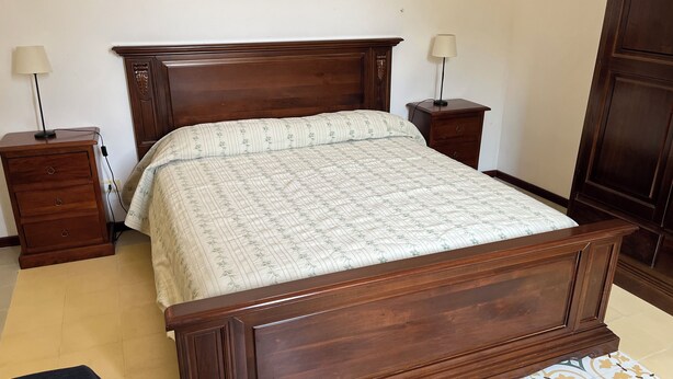 Un lit en bois avec une couvre-lit à motifs floraux, deux tables de chevet avec des lampes et une armoire en bois.