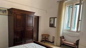 Une chambre à coucher comprenant un lit, une armoire, une petite table, une chaise et une fenêtre avec des rideaux.