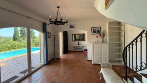 A spacious room with a large sliding glass door leading to a swimming pool, a chandelier, a white console table, and a staircase with a metal railing. - Provencal villa for 10 people with swimming pool and garden in Grasse (Grasse)