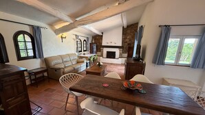A cozy living area with a wooden dining table, white chairs, a leather sofa, and a stone fireplace. - Provencal villa for 10 people with swimming pool and garden in Grasse (Grasse)