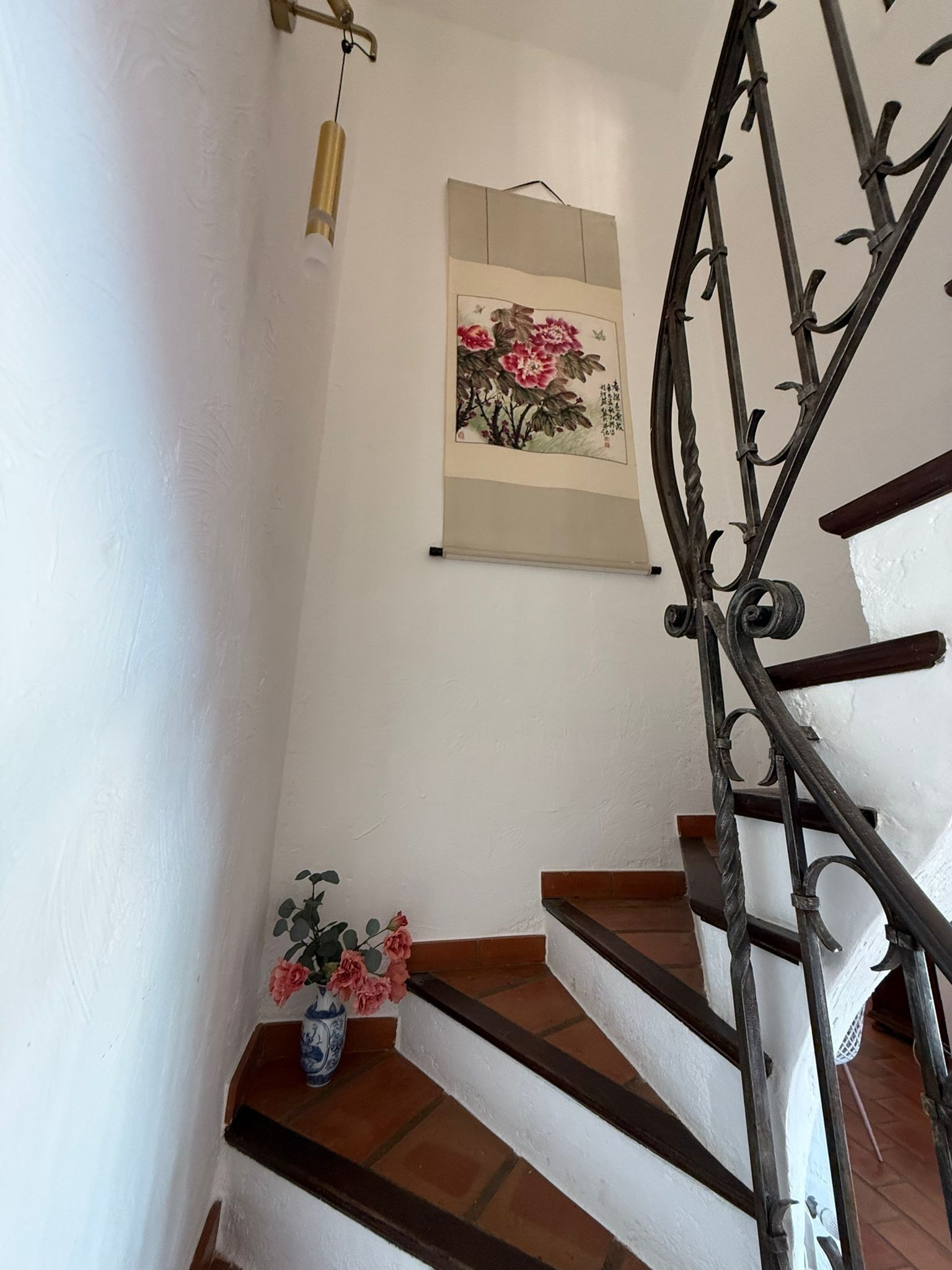 A staircase with a metal railing, a vase with flowers, and a framed artwork on the wall.