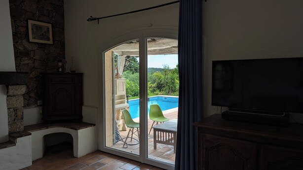 A room with a stone wall, a fireplace, a television, and a sliding glass door leading to a pool area with chairs. - Provencal villa for 10 people with swimming pool and garden in Grasse (Grasse)