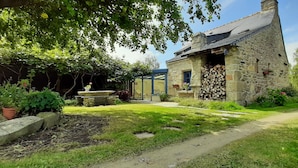 A stone building with a sloped roof, a covered outdoor seating area, and a garden with potted plants and a pathway. - Fisherman's cottage Seasonal rental July (Piriac-sur-Mer)