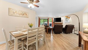 A dining area with a wooden table and chairs, a ceiling fan, a painting on the wall, and a view of the outdoors through a window. - Updated 2 bedroom walk-in with 2 king beds in Pointe Royale Golf Village (Branson)