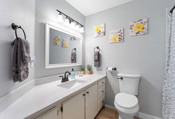 A modern bathroom with a white sink, a toilet, and a mirror. There are towels hanging on a rack and a potted plant on the counter.