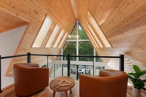 Interior de madera con techo alto y ventanas amplias, que incluye una zona de estar con vistas al exterior.