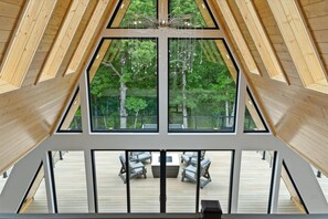 Un interior moderno con techo alto, ventanas amplias y vistas a una terraza exterior con mobiliario.