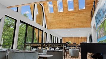 A modern interior with large windows, wooden ceiling, and a dining area with grey furniture.