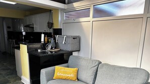 Ett modernt kök med en grå soffa och en gul kudde, en korg och en hängande växt.