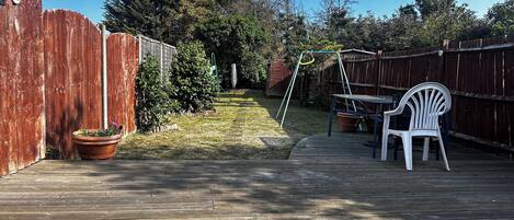 A wooden deck with a swing set, a white plastic chair, and a potted plant.