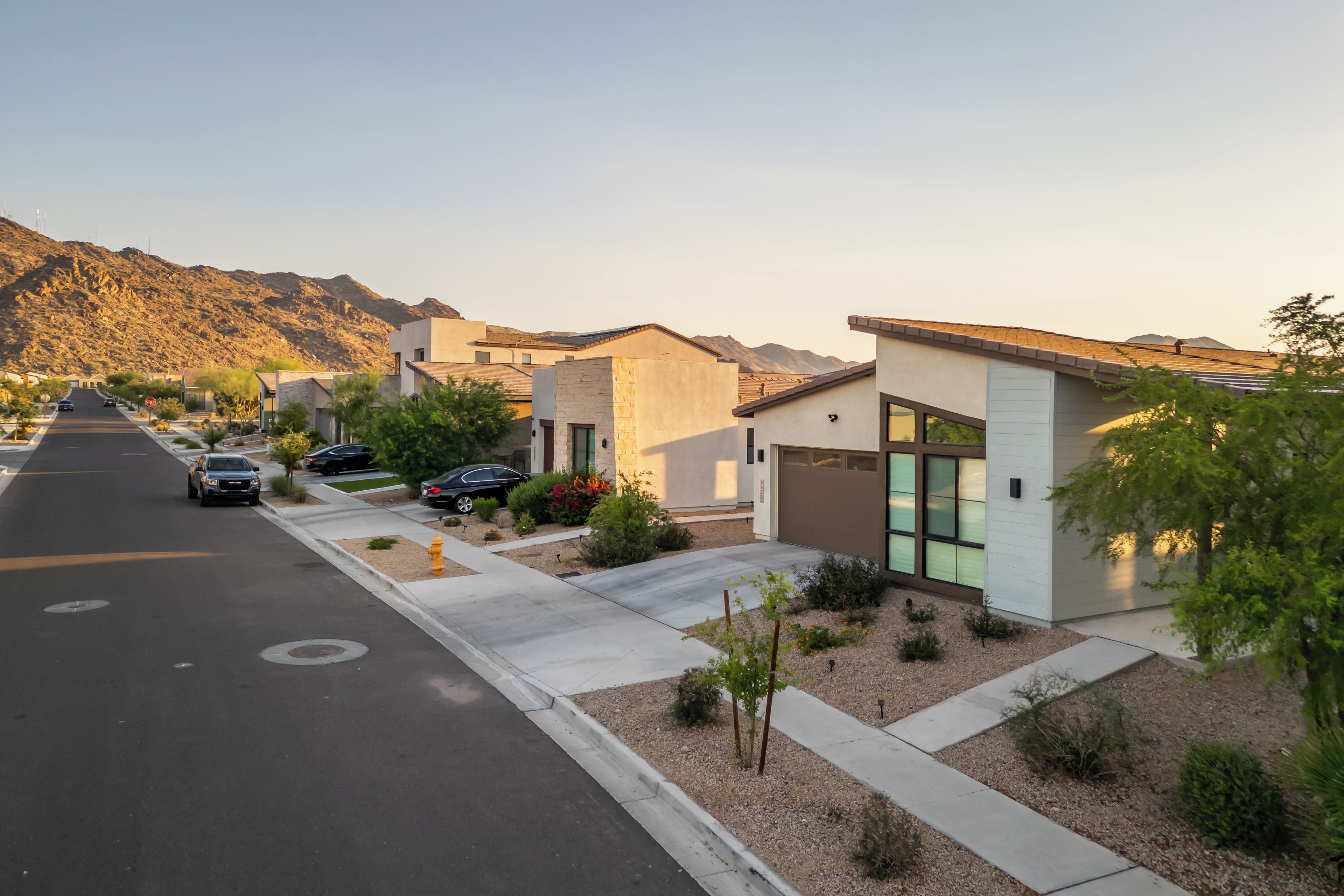 Una calle residencial con casas modernas, cielo despejado y montañas al fondo.