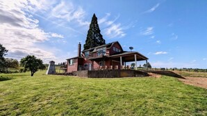 Una casa grande de dos pisos con una chimenea destacada, un porche cubierto y un césped bien cuidado.