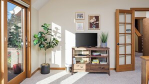 Un salón con televisor sobre un mueble de madera, una planta en maceta y un ventanal corredera que da a un balcón.
