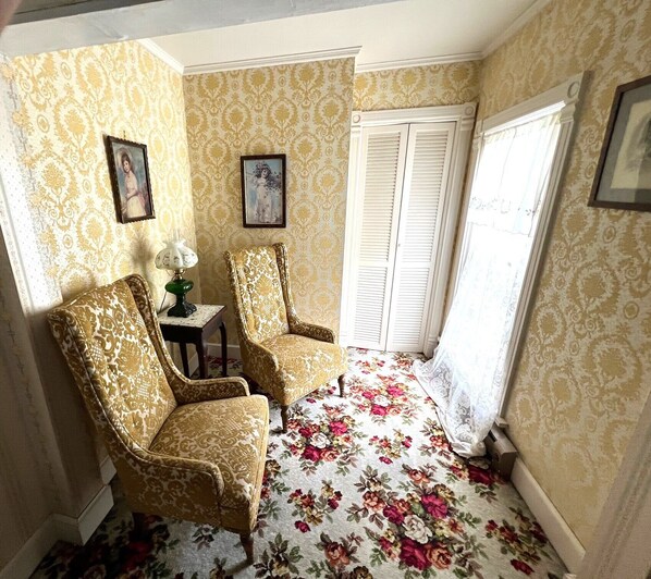A room with two patterned armchairs, a small table with a lamp, floral carpet, patterned wallpaper, and a window with shutters. - Greyhouse Inspirational Retreat - B&B Experience (Salmon)