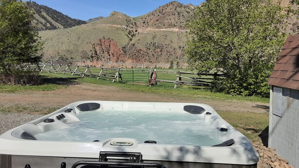 Un jacuzzi en un entorno rural, con una valla de madera y montañas al fondo.