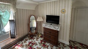 Una habitación con una televisión sobre una cómoda, un espejo, una lámpara y alfombra estampada con motivos florales.