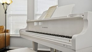 A white grand piano with a music stand and sheet music titled "CHOPIN" in a room with white walls and a window with blinds.