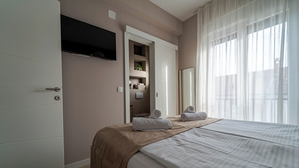 A bedroom with a bed, a TV mounted on the wall, a wardrobe, and a bathroom with a shower and a towel rack. - Spacious 3-bedroom apartment in Sukosan (Sukošan)