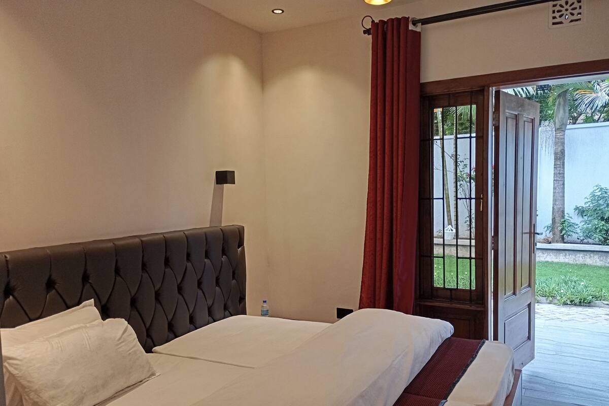 A hotel room with a large bed, a nightstand, a window with a view of the outdoors, and a door leading to a balcony.