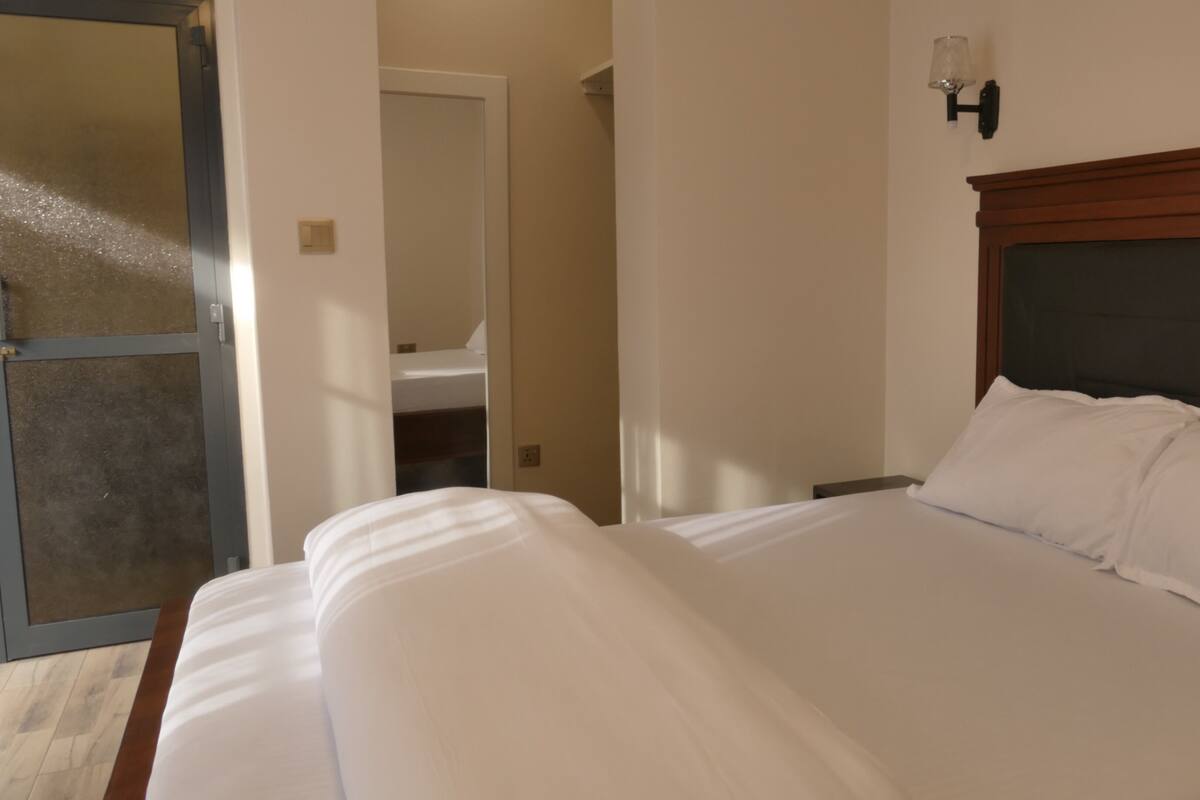A hotel room with a large bed, a wooden headboard, and a wall-mounted light fixture.