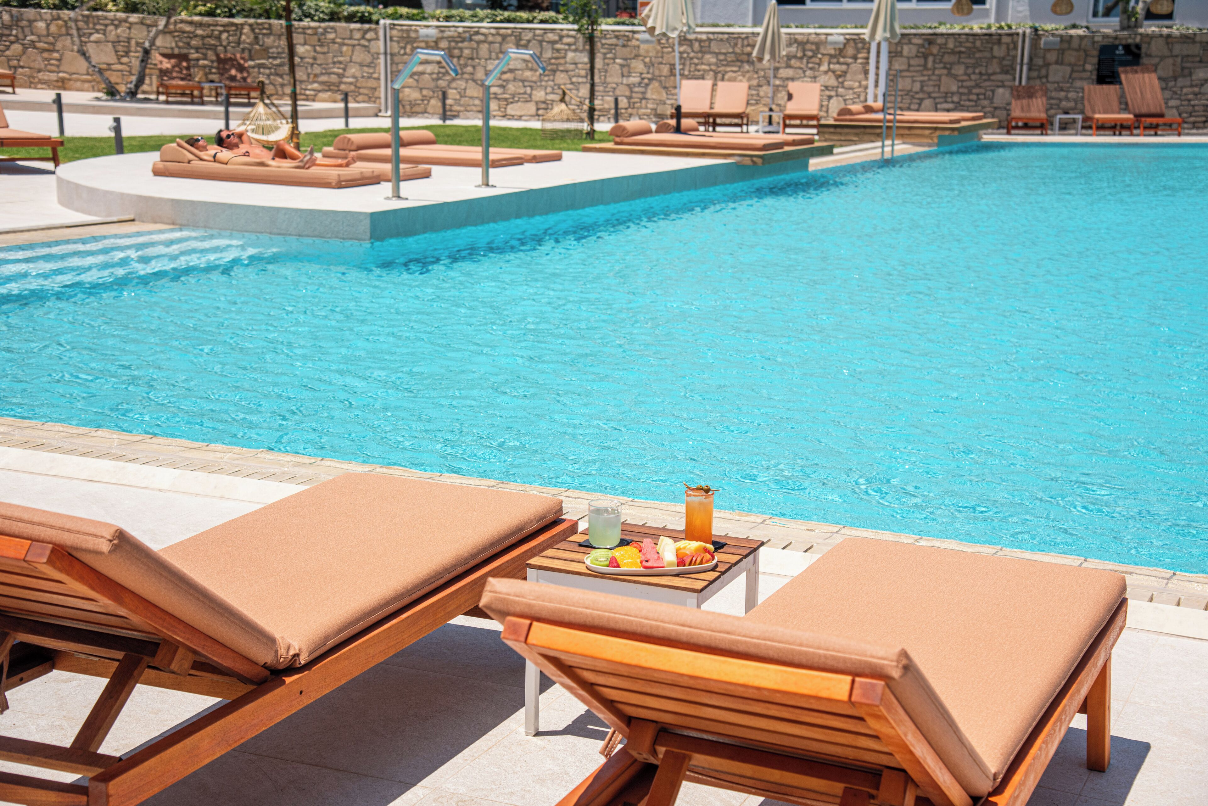 A poolside area with lounge chairs and a table with a plate of food and drinks.