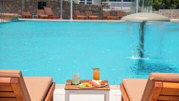 A poolside view with lounge chairs, a table with a fruit platter and drinks, and a water feature.