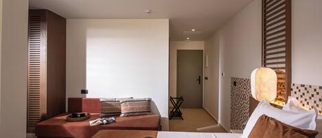 A modern hotel room with a bed, a sofa, and a small table. There is a hat and a magazine on the table.