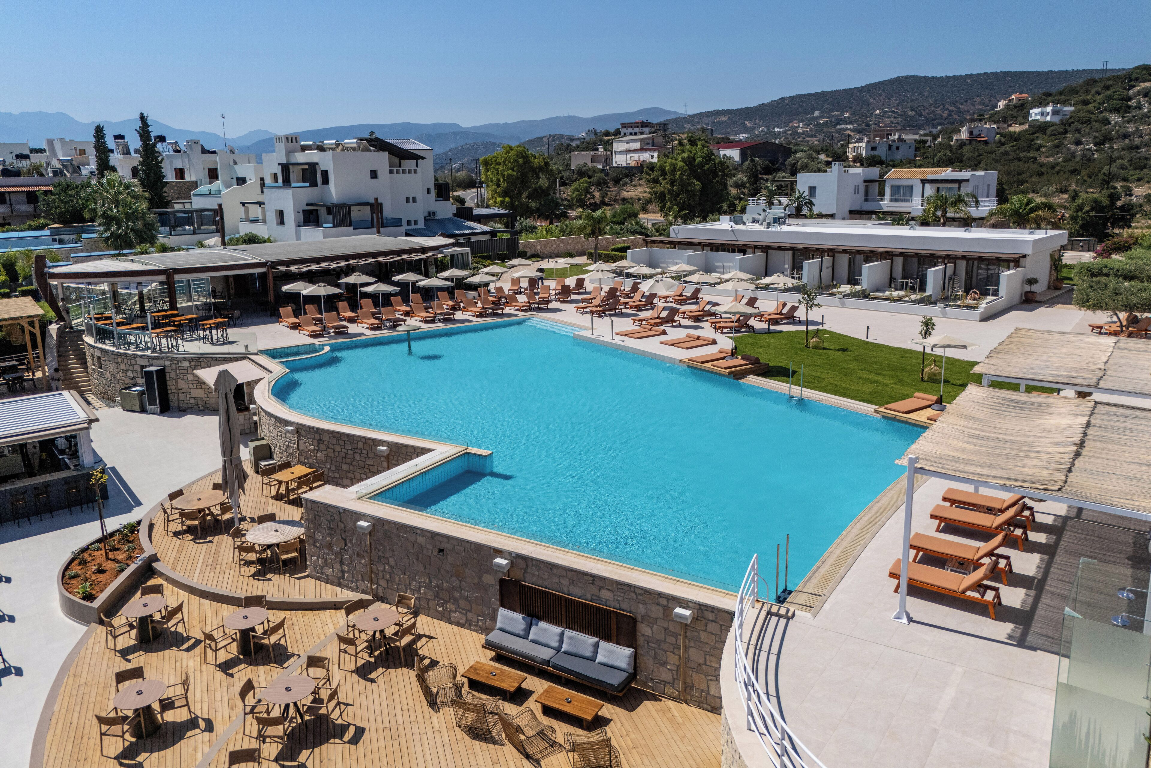 A rooftop pool area with lounge chairs and a swimming pool, surrounded by modern buildings and a view of the hills.