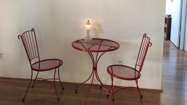 A room with a desert-themed wall art, a small table with a lamp, and two red metal chairs. - Wild Goose Ranch (Homestead Valley)