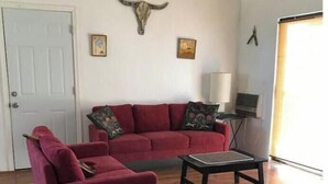 A living room with a red sofa, a matching armchair, a coffee table, and a wall-mounted bull's head decoration. - Wild Goose Ranch (Homestead Valley)